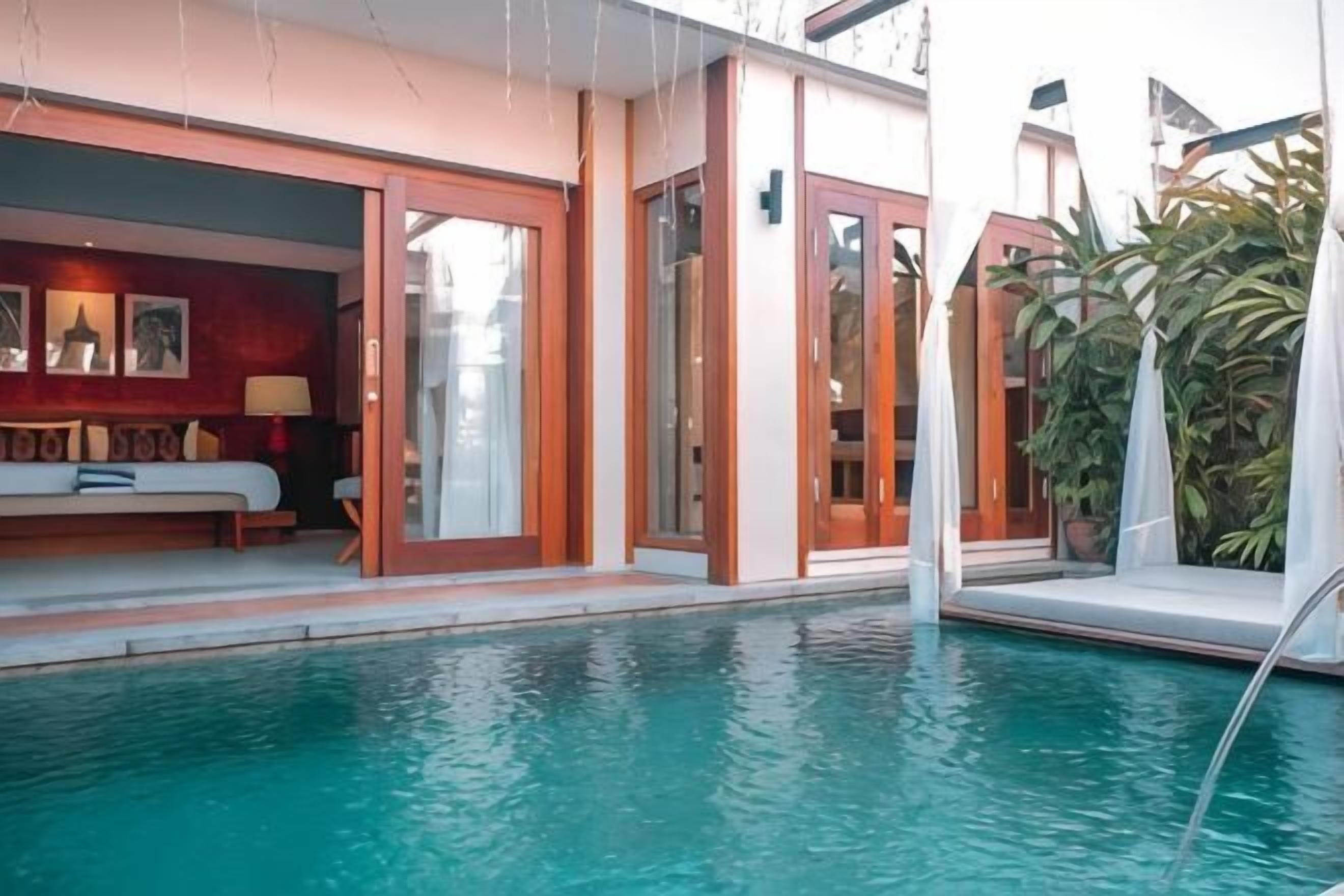 A poolside area with a lounge chair, a sofa, and a glass door leading to a room.
