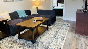 Un salon avec un canapé foncé, une table basse en bois et un tapis à motifs.