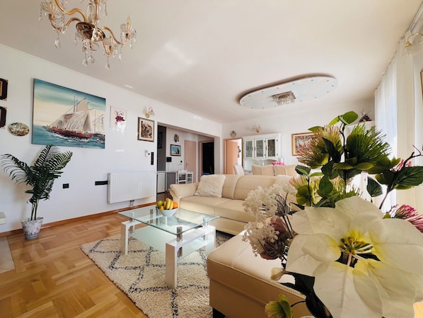Una sala de estar moderna con una mesa de centro de vidrio, sofá color beige y un área de comedor al fondo.