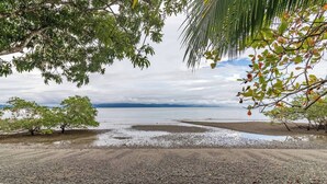 A beach with pebbles, trees, and a calm sea under a cloudy sky.