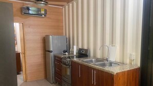 A compact kitchen with wooden cabinets, a stainless steel refrigerator, a stove, and a sink.