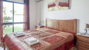 Habitación de hotel con una cama grande, una mesita de noche con lámpara, una ventana con cortinas y un cuadro en la pared.