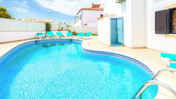 Una piscina con borde de azulejos, rodeada de sillas de descanso y una terraza con baldosas.