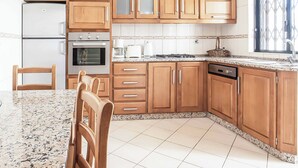 Una cocina con armarios de madera, encimera de granito, refrigerador, horno, lavavajillas y una ventana con celosía decorativa.