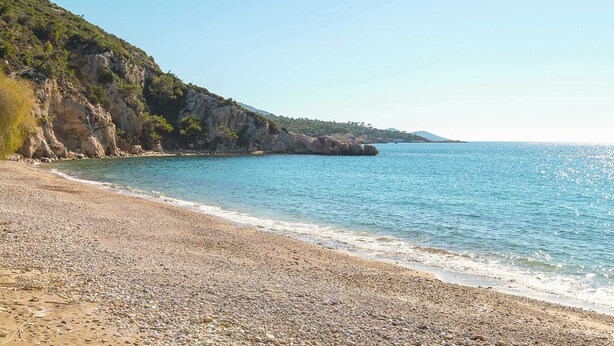 Ein Kiesstrand mit einer felsigen Klippe und klarem, blauem Meer.