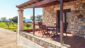 Ein Steinhaus mit einer überdachten Terrasse, Sitzgelegenheiten im Freien und Blick auf das Meer.