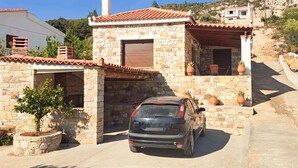 Ein Haus aus Stein mit Ziegeldach und Schornstein, davor ein geparktes Auto.