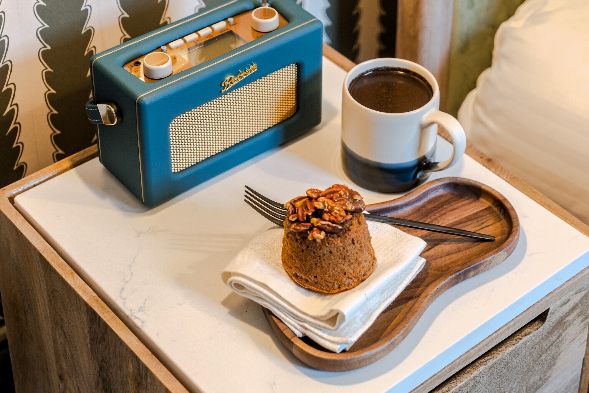 A breakfast tray with a muffin topped with pecans, a cup of coffee, and a vintage radio.