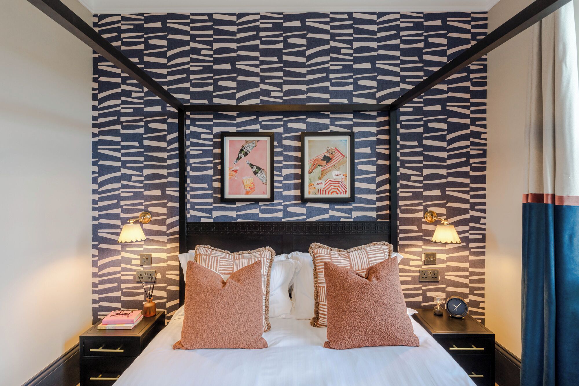 A hotel room with a zebra-striped wall, a bed with two pillows, two bedside tables with lamps, and two framed pictures on the wall.