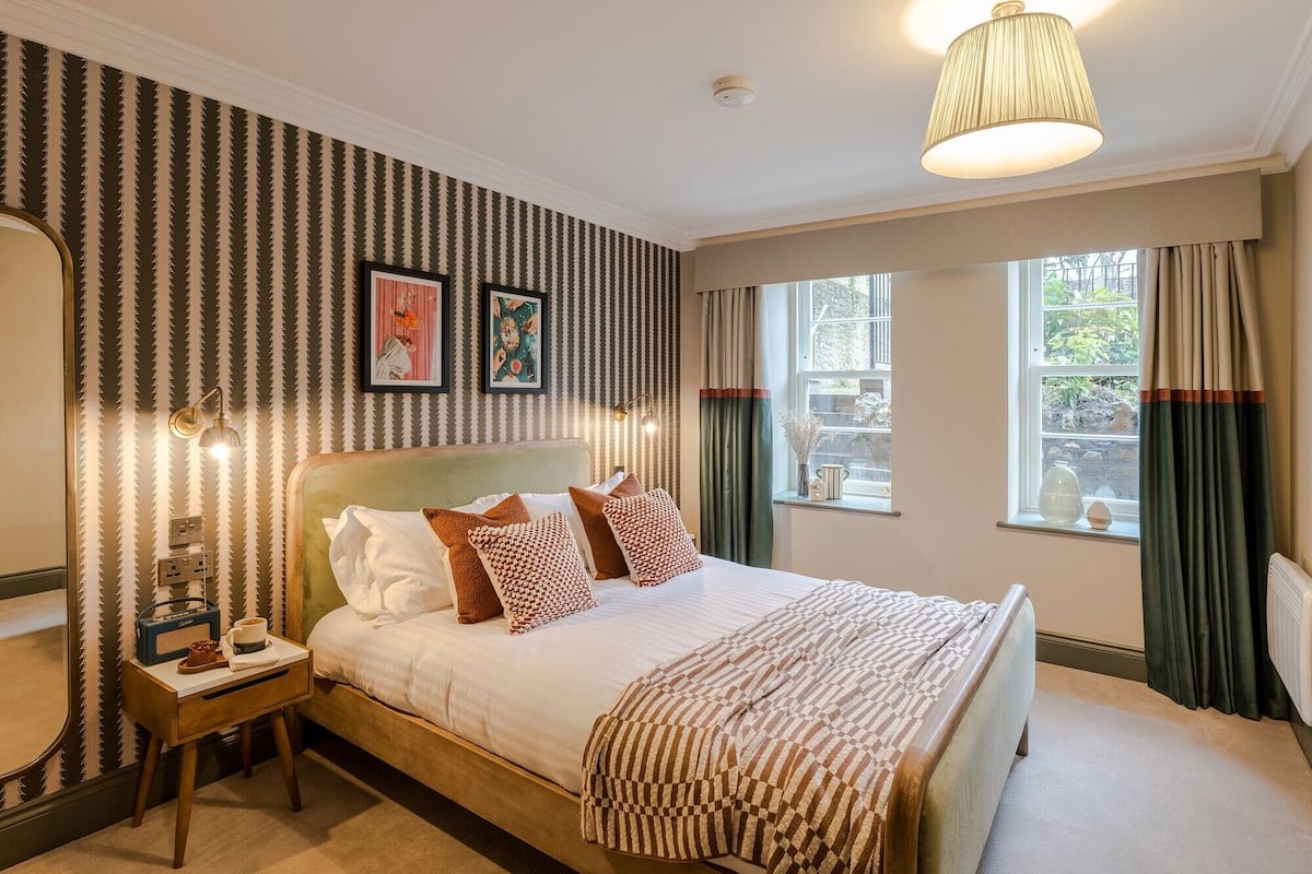 Quarto com cama grande, mesa de cabeceira, abajur e janela com cortinas.