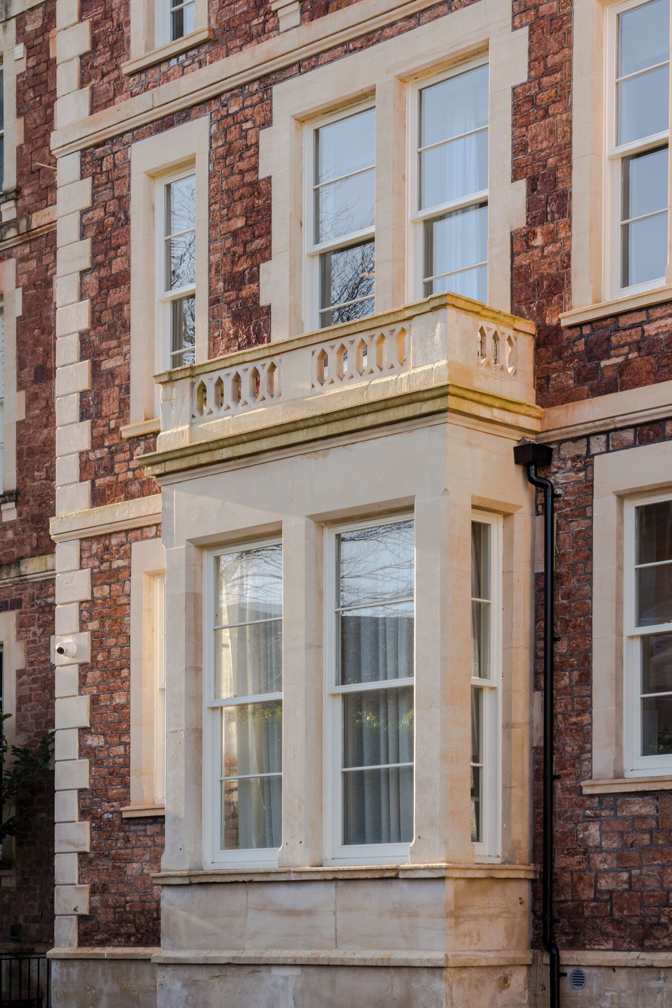A corner bay window with white frames and a decorative balustrade, set in a brick building with multiple windows.