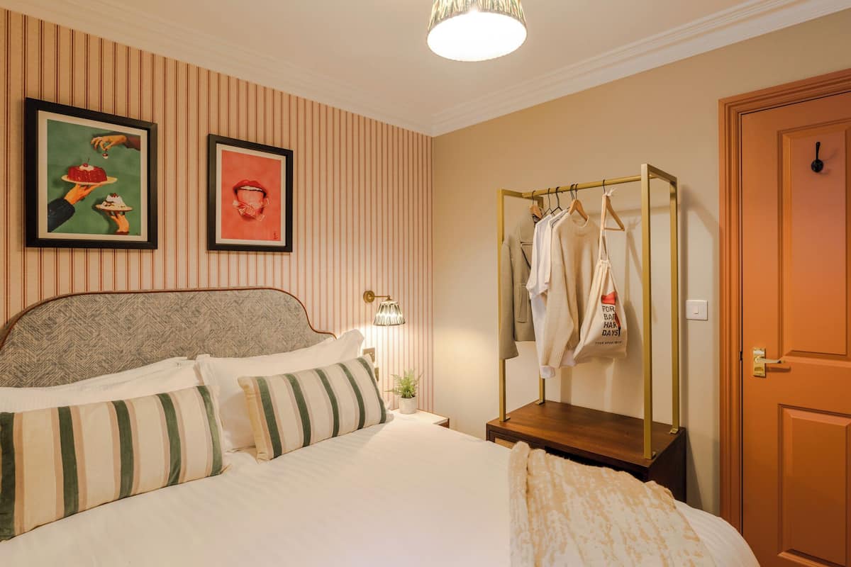 Quarto bem arrumado com cama, mesa de cabeceira com abajur, guarda-roupa e duas fotos emolduradas na parede.