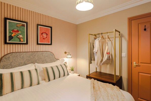 Un dormitorio ordenado con una cama, una mesita de noche con lámpara, un armario y dos cuadros en la pared.
