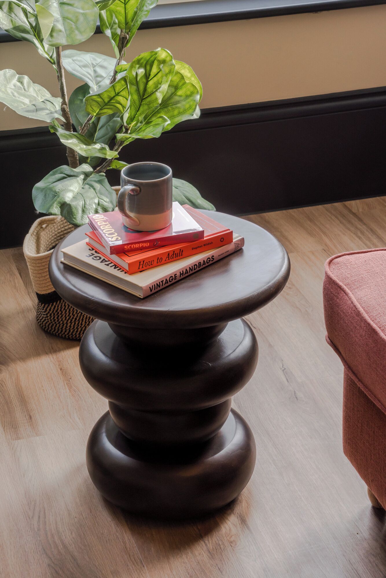 A round wooden table with a stack of books and a mug on top.