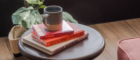 A round wooden table with a stack of books and a mug on top.