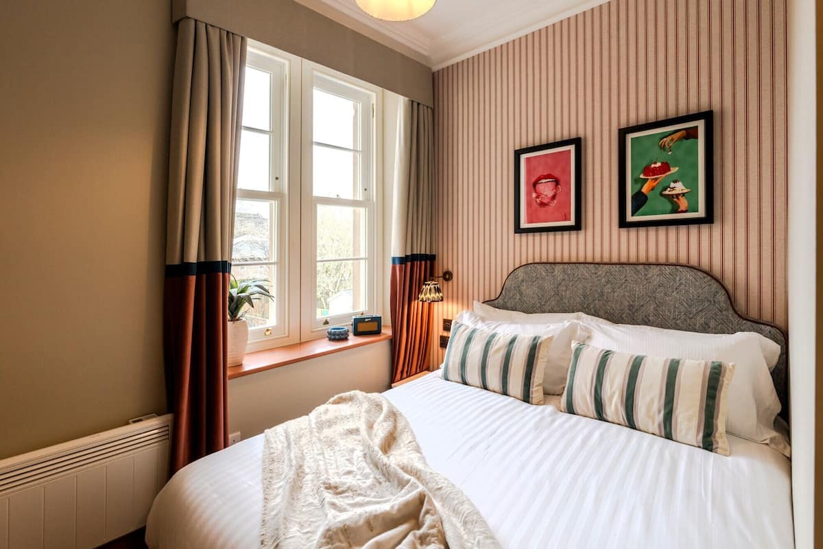 Um quarto com uma cama, uma janela com cortinas e duas molduras na parede.