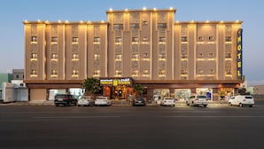 Ein Hotel mit mehreren Etagen, einem markanten Eingang und einigen Autos vor der Fassade.