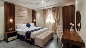 Ein modernes Hotelzimmer mit einem großen Bett, einem hölzernen Kopfteil, einem Nachttisch, einem Stuhl und einem kleinen Tisch mit einer Blumenvase.