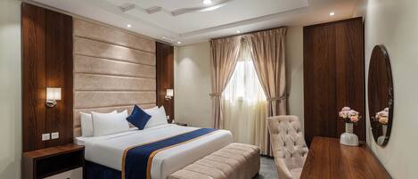 Una habitación de hotel moderna con una cama grande, un cabecero de madera, una mesita de noche, una silla y una pequeña mesa con un jarrón de flores.