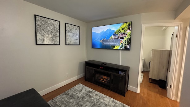 A living room with a flat-screen TV mounted on the wall, a fireplace, and two framed maps. - Extended Stay Studio Apartment in Thunder Bay (Thunder Bay)