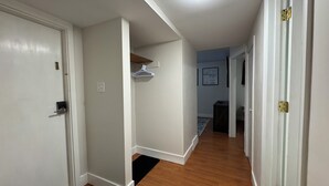 A hallway with white walls, a wooden floor, and a ceiling light. There are doors on both sides, a black doormat, and a white door with a lock. - Extended Stay Studio Apartment in Thunder Bay (Thunder Bay)
