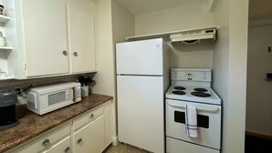 A compact kitchen with white cabinets, a microwave, a refrigerator, and a stove. - Extended Stay Studio Apartment in Thunder Bay (Thunder Bay)