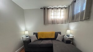 A modern living room with a grey sectional sofa, a yellow throw blanket, two side tables with lamps, and a grey shag rug. - Extended Stay Studio Apartment in Thunder Bay (Thunder Bay)