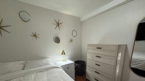 A bedroom with a bed, a dresser, a nightstand, a lamp, and wall decorations. - Extended Stay Studio Apartment in Thunder Bay (Thunder Bay)