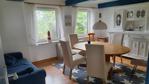 Huone, jossa on ruokapöytä, tuoleja, sohva, ikkuna verhoilla, patteri ja seinä, jossa on koriste-esineitä.