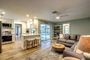 A modern kitchen with a central island, a dining area with a grey sofa, and a view of a swimming pool.
