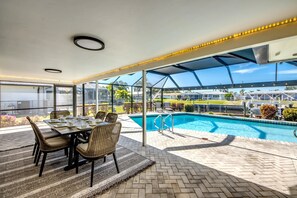 A covered outdoor area with a pool, dining table, and chairs.