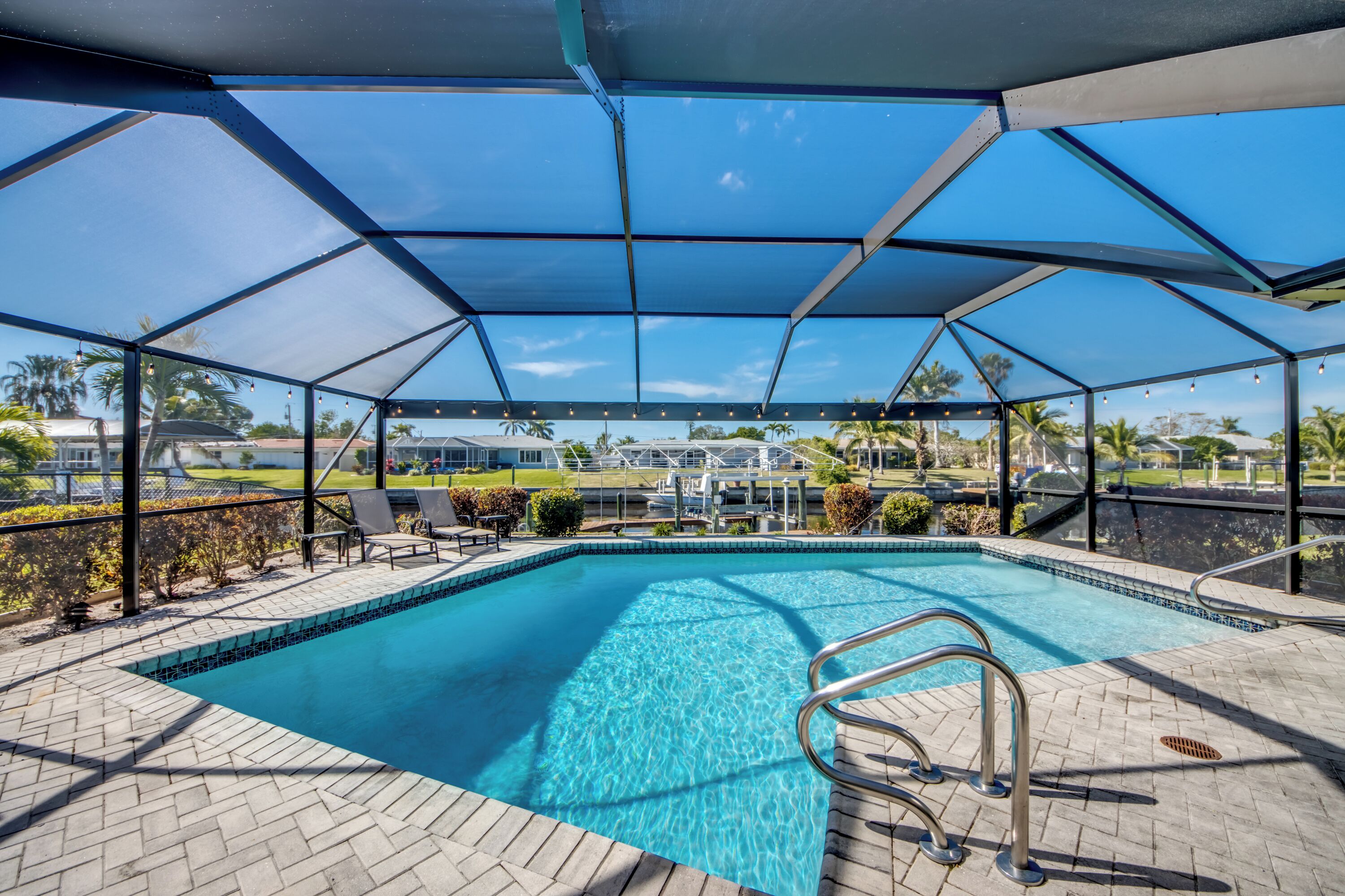 A covered swimming pool with clear blue water, surrounded by a brick patio and a metal fence.
