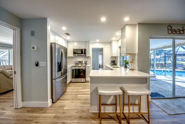 A modern kitchen with stainless steel appliances, a central island with bar stools, and a view of a swimming pool.