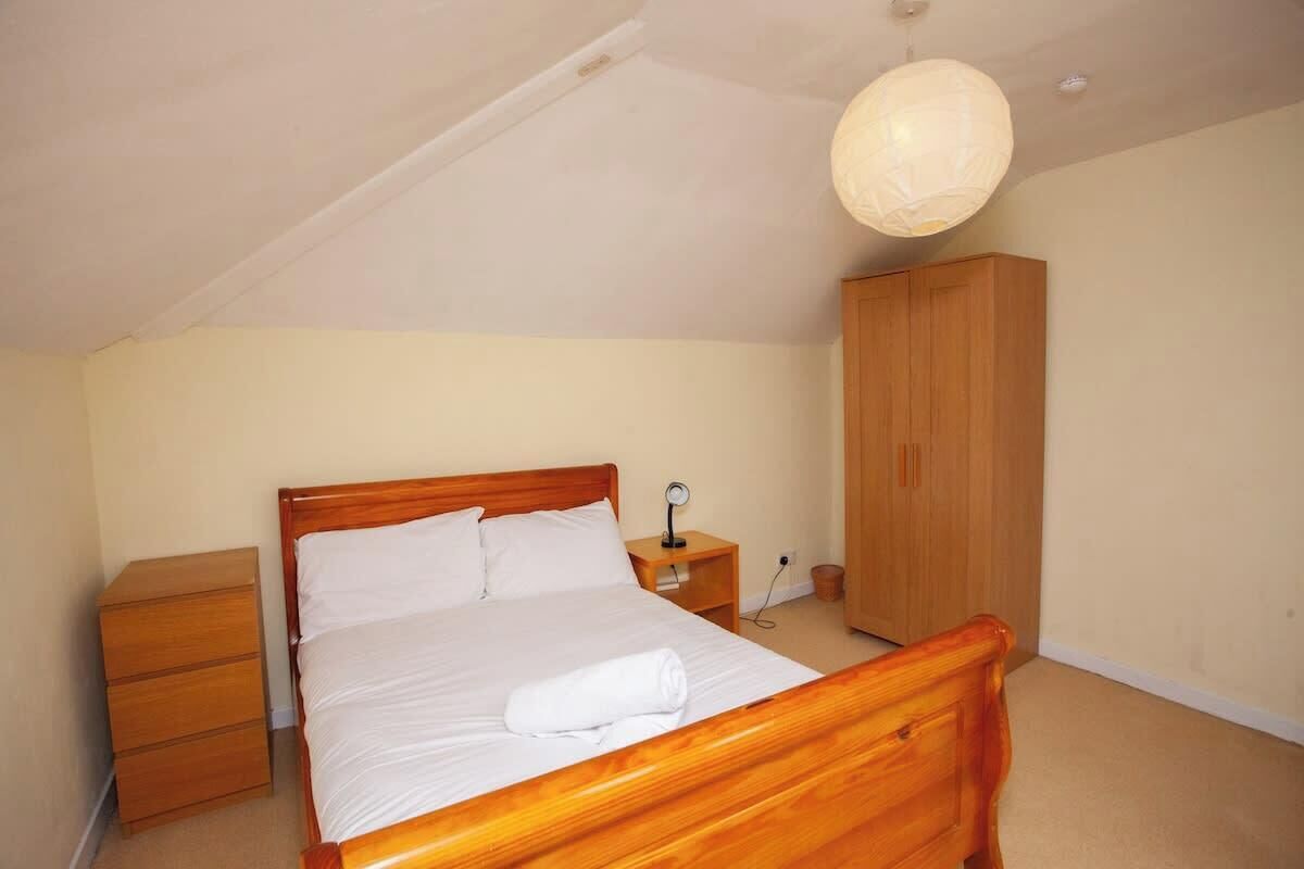 Ein Schlafzimmer mit einem hölzernen Bett, einem Nachttisch, einem Kleiderschrank und einer Hängelampe.