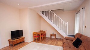 Een woonkamer met een houten vloer, een bank, een tv-meubel, een eettafel met stoelen en een trap.