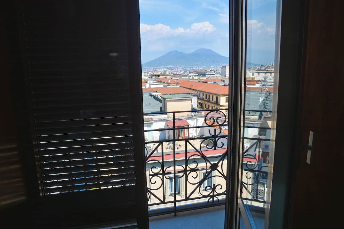 A view from a balcony with a metal railing, overlooking a cityscape with buildings and a mountain in the distance.