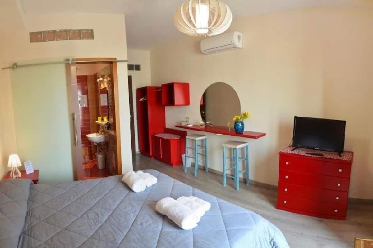 A bedroom with a bed, a TV, a red dresser, and a bathroom visible through an open door.