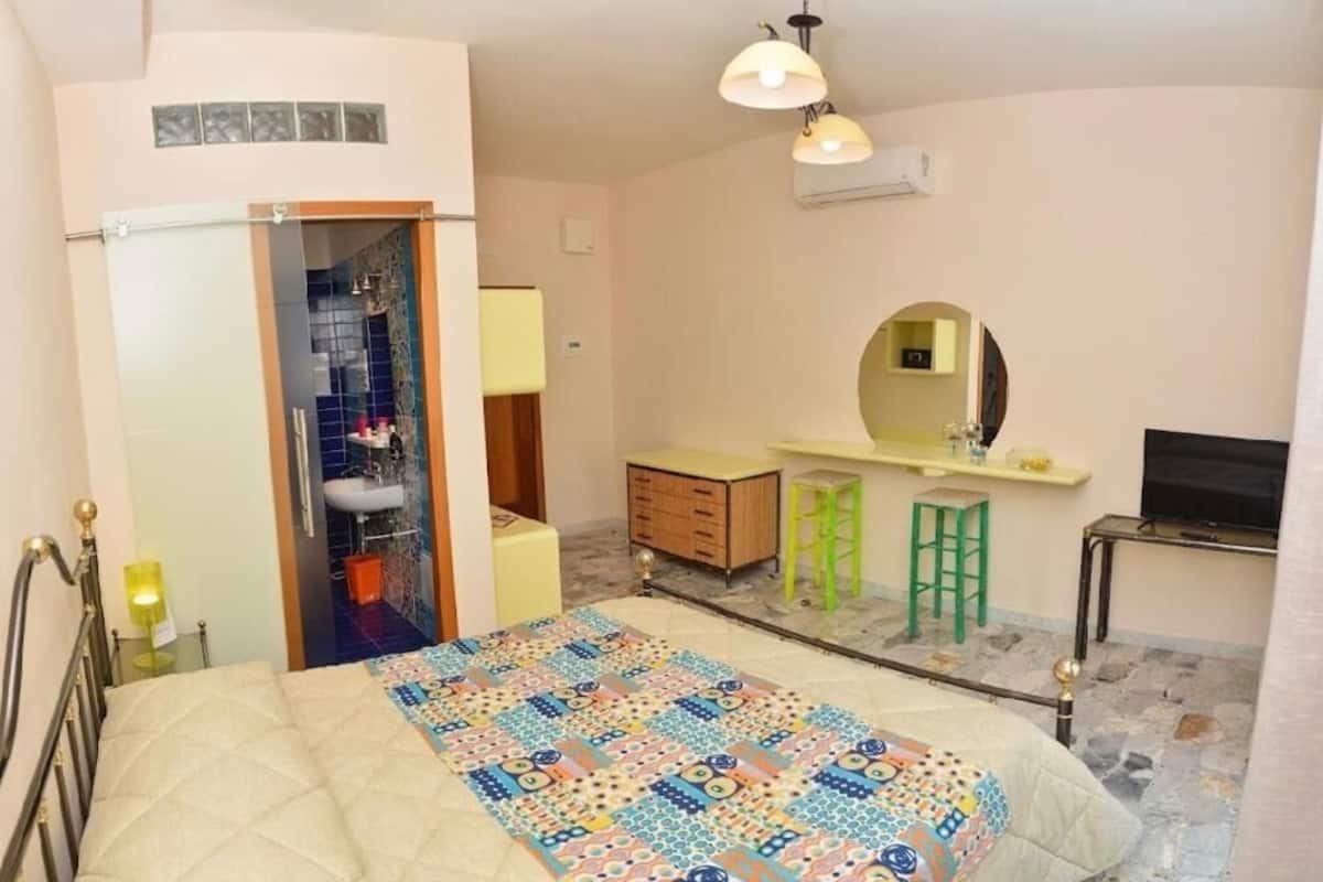 A bedroom with a bed, a bathroom with a sink, a mirror, and a TV.