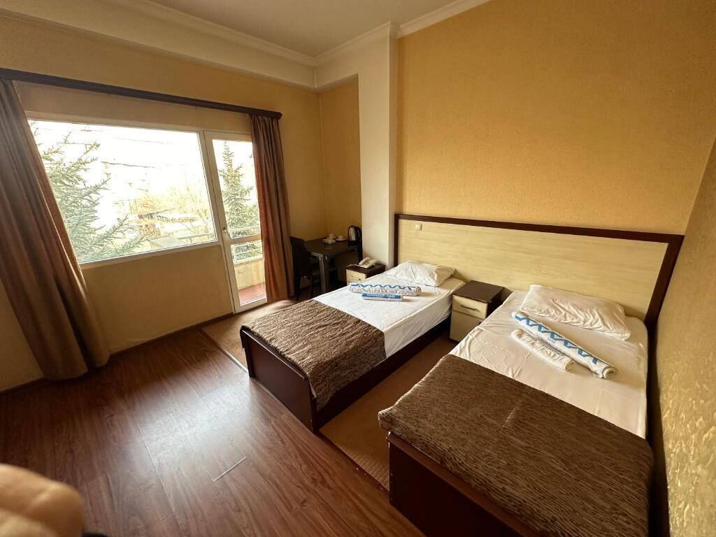 Una camera d'albergo con due letti, una scrivania e una finestra con tende.