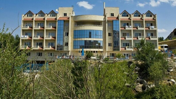Un hotel de diverses plantes amb un atrium central, balcons a cada planta i un paisatge natural al voltant.