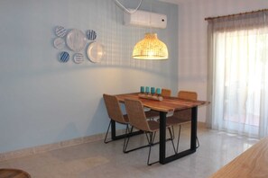 A dining area with a wooden table, four chairs, a hanging pendant light, and wall decor. - Seahorse House, T2 Tavira – Santa Luzia (Caminho das Trindades)
