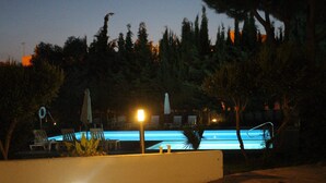 Ein Poolbereich bei Nacht mit Liegestühlen, einem Pool und einem Halbmond am Himmel.
