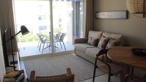 A living room with a sofa, a dining table, a lamp, and a view of the outside balcony.