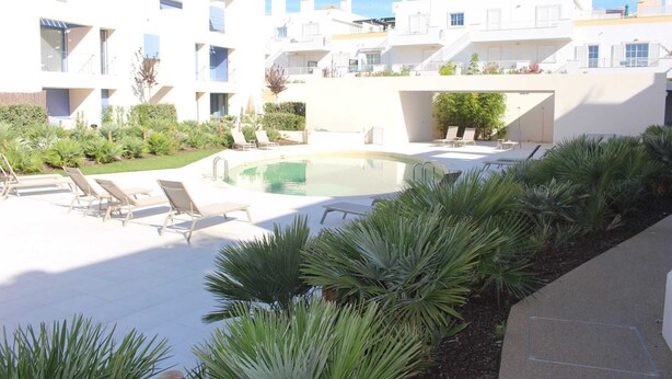 A modern building with a swimming pool, sun loungers, and a well-maintained garden.