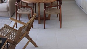 A dining area with a round wooden table, wicker chairs, and a hanging light fixture.