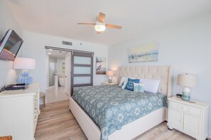 A bedroom with a bed, nightstands, a ceiling fan, a TV, and a door leading to a bathroom. - Gulf-front 3BR corner unit, updated, balconies, Pool and Hot Tub! (Destin)