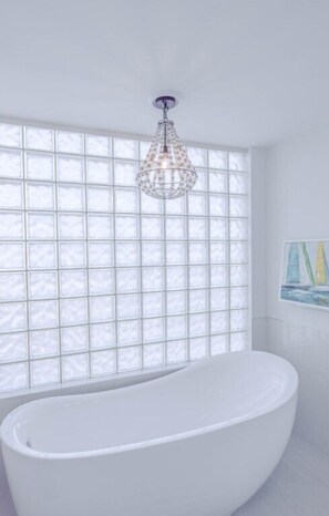 A modern bathroom with a freestanding bathtub, a large window with a grid pattern, and a hanging light fixture. - Gulf-front 3BR corner unit, updated, balconies, Pool and Hot Tub! (Destin)