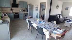 Une cuisine moderne avec des meubles de couleur bleu clair, une table à manger recouverte d’une nappe à motifs et un poêle noir.