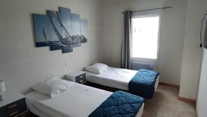 Une chambre d’hôtel avec deux lits simples, un petit bureau avec une chaise, une table de chevet et une œuvre d’art accrochée au mur.