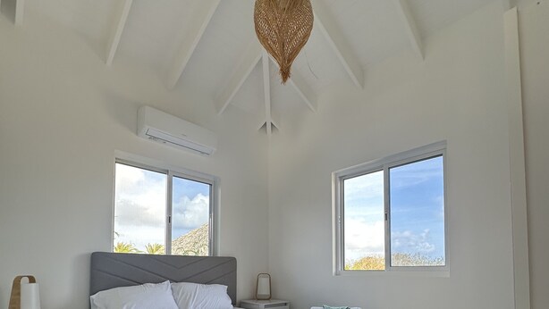 A modern bedroom with a large bed, two bedside tables, a nightstand, and a ceiling fan.